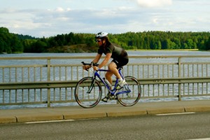photograph of chris southwell cycling on a road with lake and trees in the background
